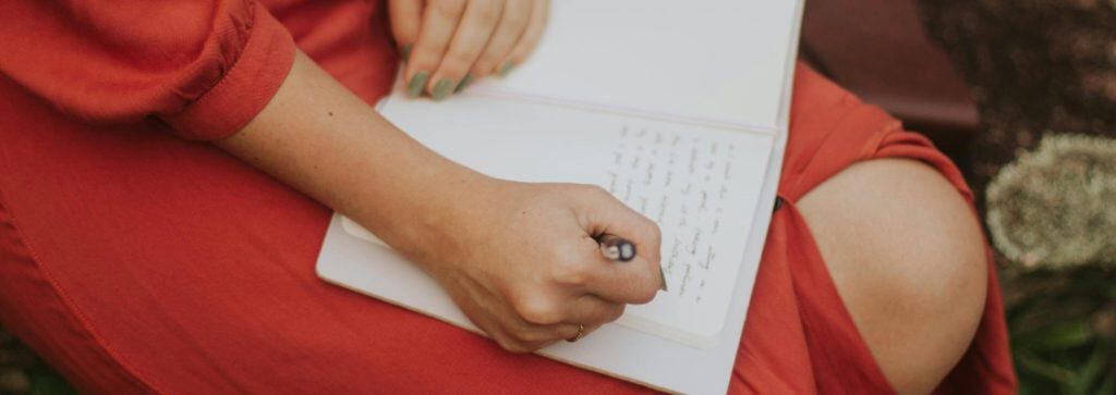 foto van een vrouw in een rode jurk die schrijft in een schrift