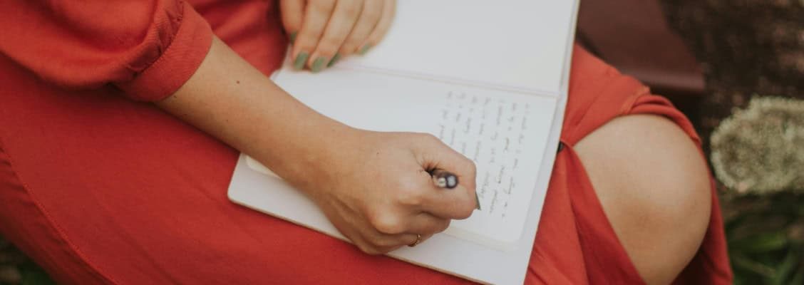 foto van een vrouw in een rode jurk die schrijft in een schrift
